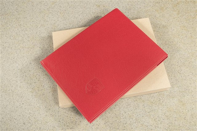 Leder-Dokumentenmappe in Rot mit geprägtem Porsche-Logo zur Aufbewahrung des Servicehefts und der Fahrerhandbücher.